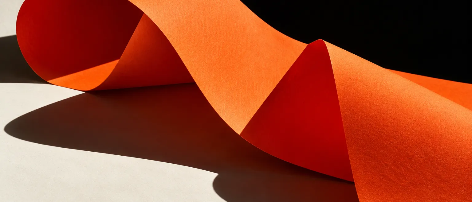 Dramatic close-up of a large sheet of signal-orange paper curling and folding in hard sunlight against deep black…