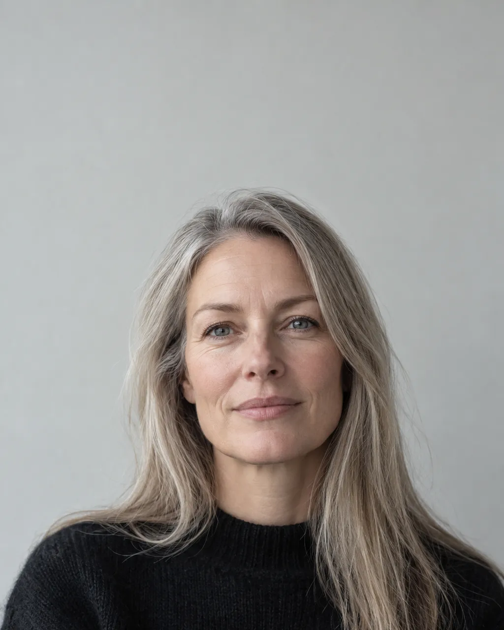 Minimal portrait of a Norwegian woman in her late forties with straight grey-blonde hair, wearing a black wool…