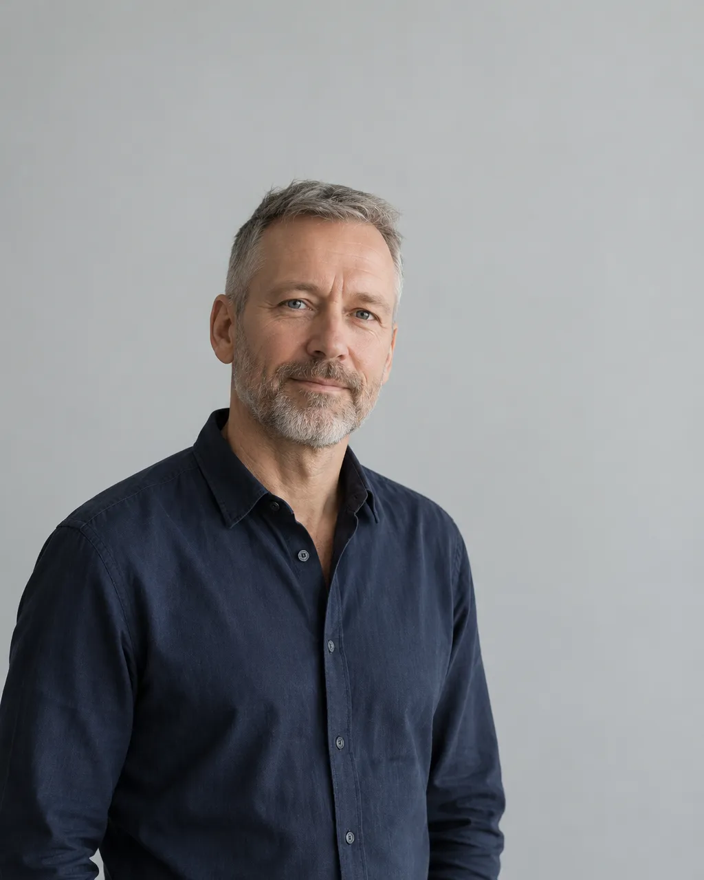 Minimal portrait of a Danish man in his early fifties with short cropped grey hair and a trimmed beard, wearing a…