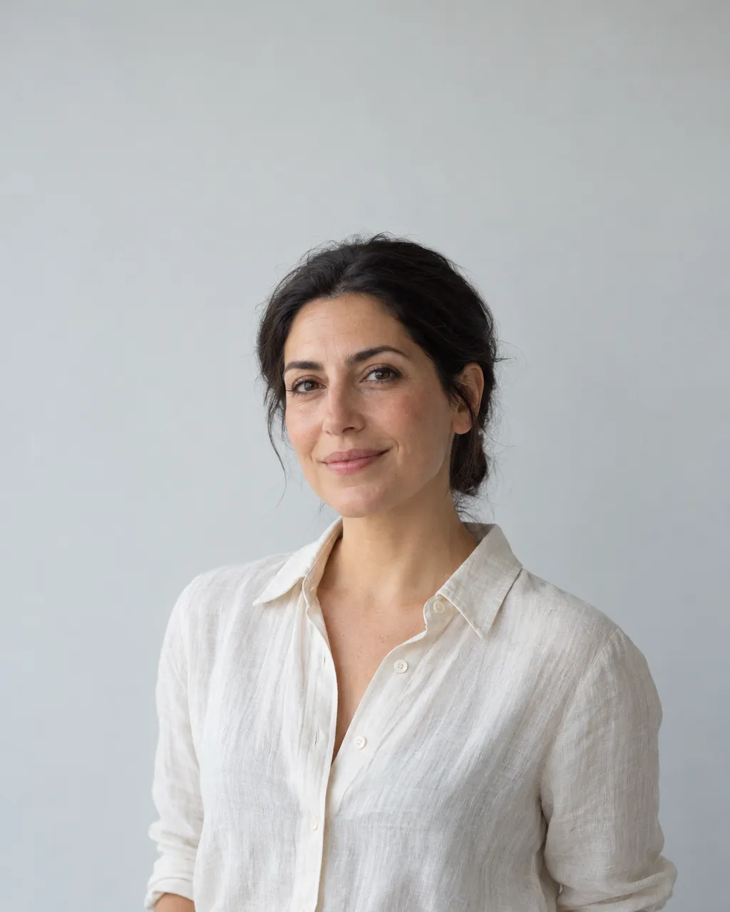 Minimal portrait of a Lebanese-Danish woman in her late thirties with dark hair pulled back, wearing a cream linen…