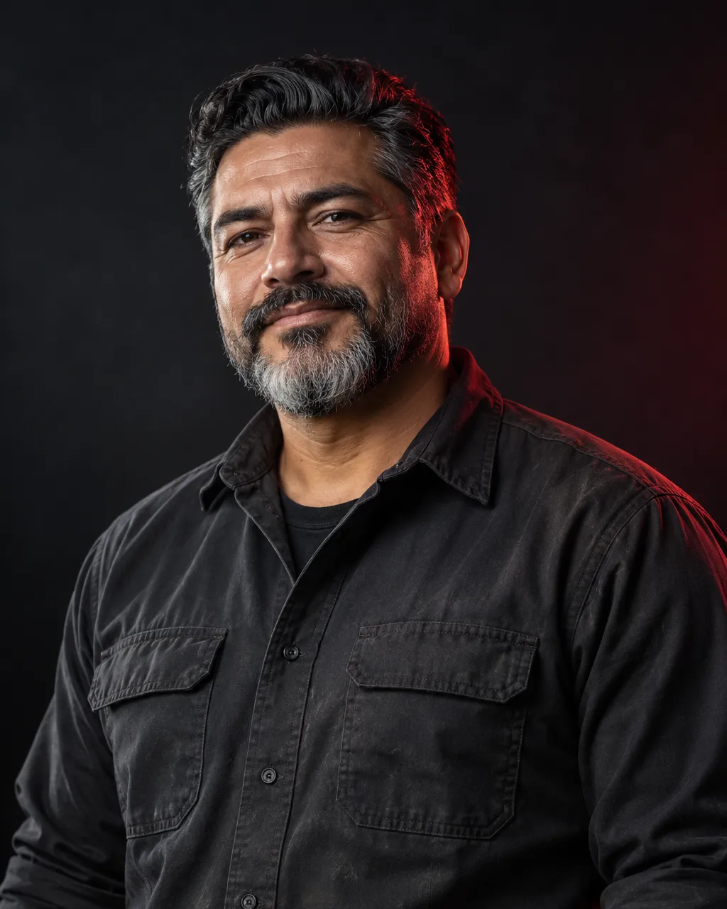 A Latino man in his late forties, founder and master mechanic, salt and pepper beard, charcoal work shirt with…