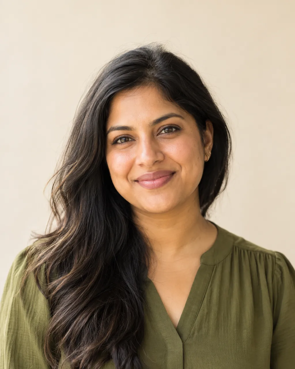 Studio-style team portrait of a South Asian woman in her thirties, community partnerships lead, long dark hair,…