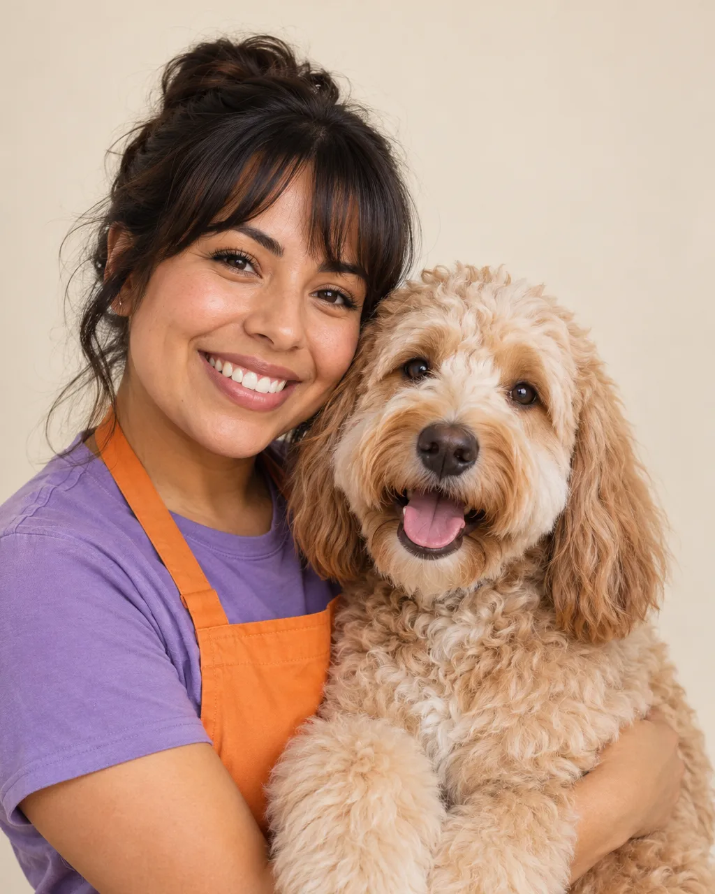 A Latina woman in her late twenties, head groomer, dark hair with bangs, violet t-shirt and tangerine apron, smiling…