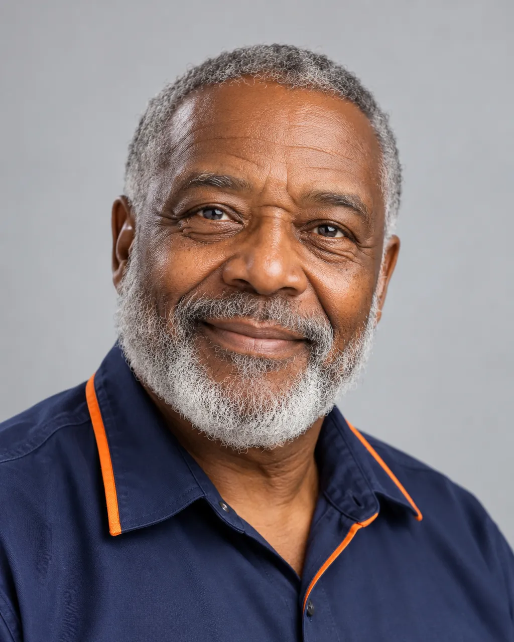 Head-and-shoulders portrait of a Black man in his late sixties with a grey beard, company founder, navy work shirt…