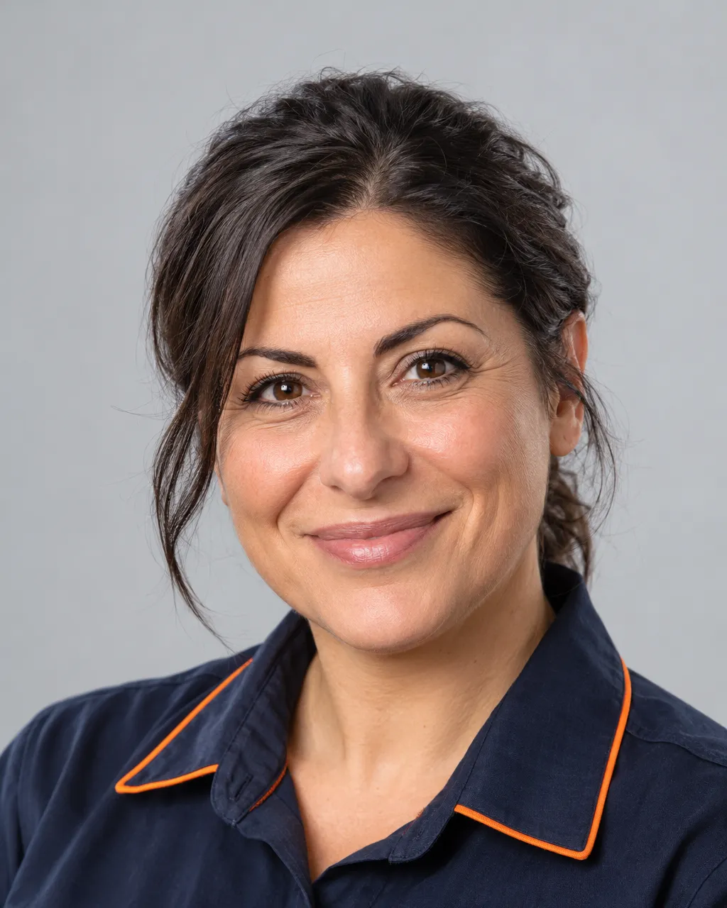 Head-and-shoulders portrait of an Italian American woman in her forties with dark hair tied back, heating manager,…