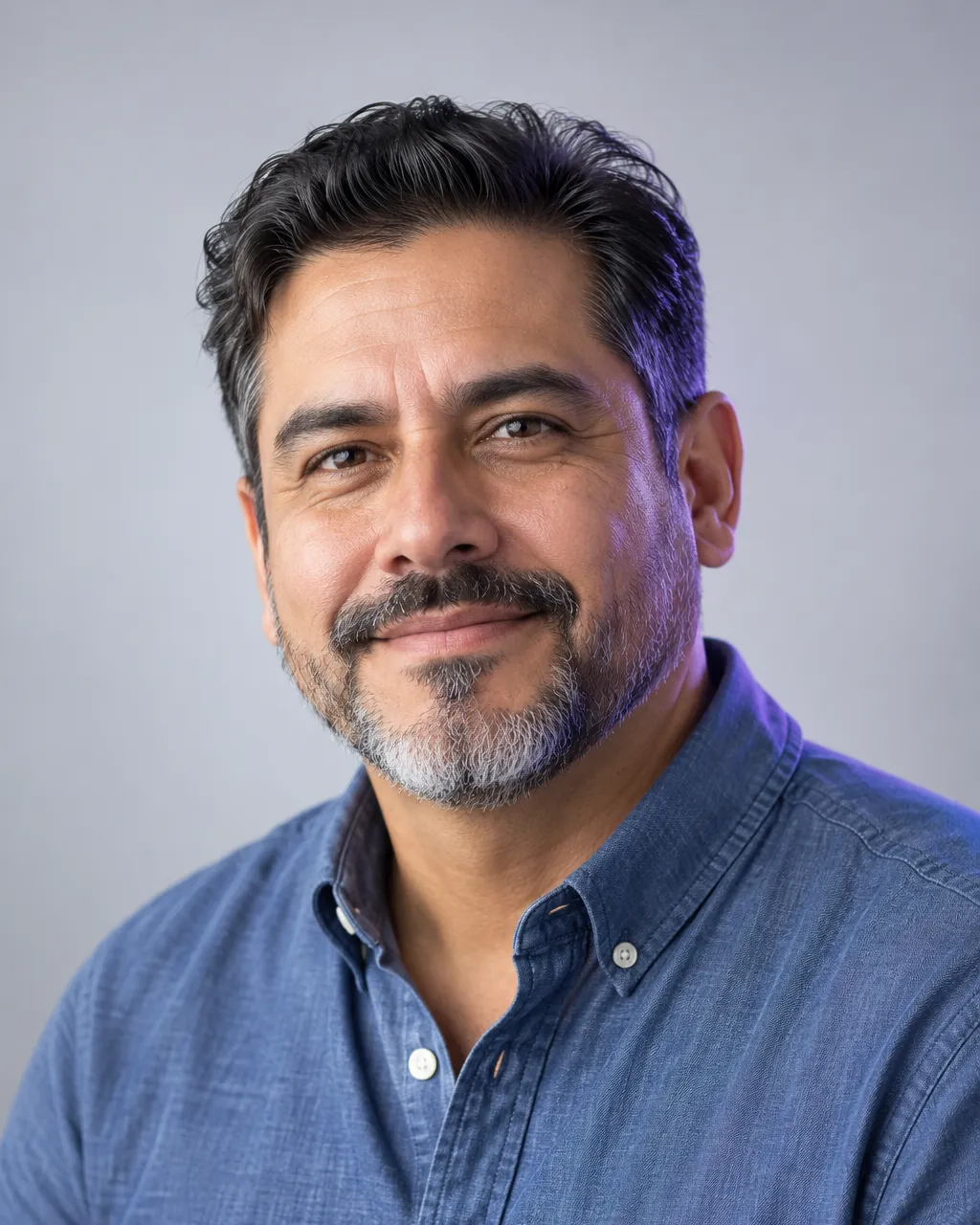 Professional head-and-shoulders portrait of a Latino man in his mid-forties with a trimmed salt-and-pepper beard,…