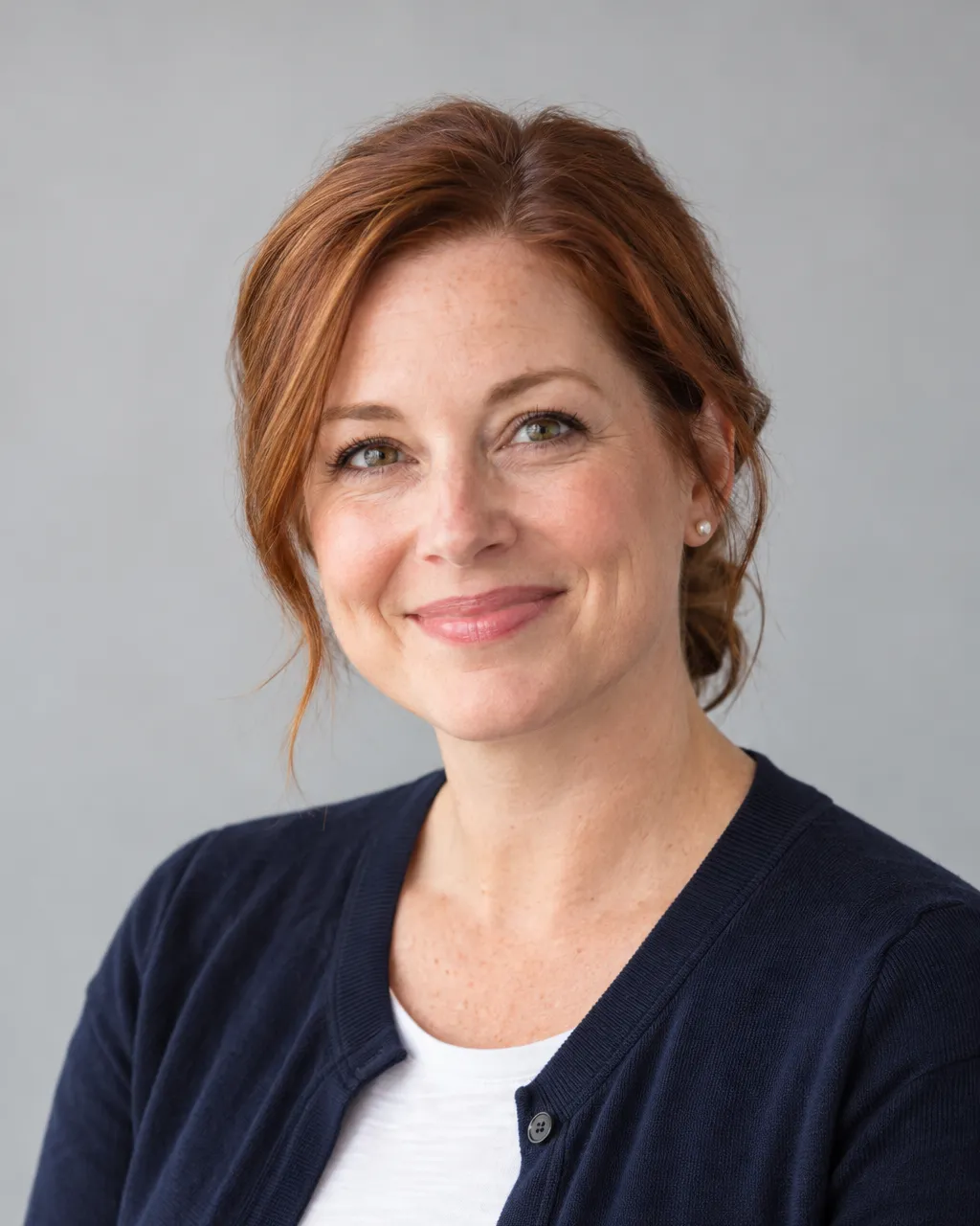 Professional portrait of a white woman in her forties, admissions director, auburn hair pulled back, navy cardigan…