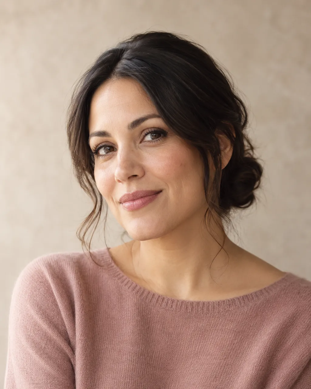 A Latina woman in her mid thirties, creative director, dark hair in a low chignon, dusty rose knit top